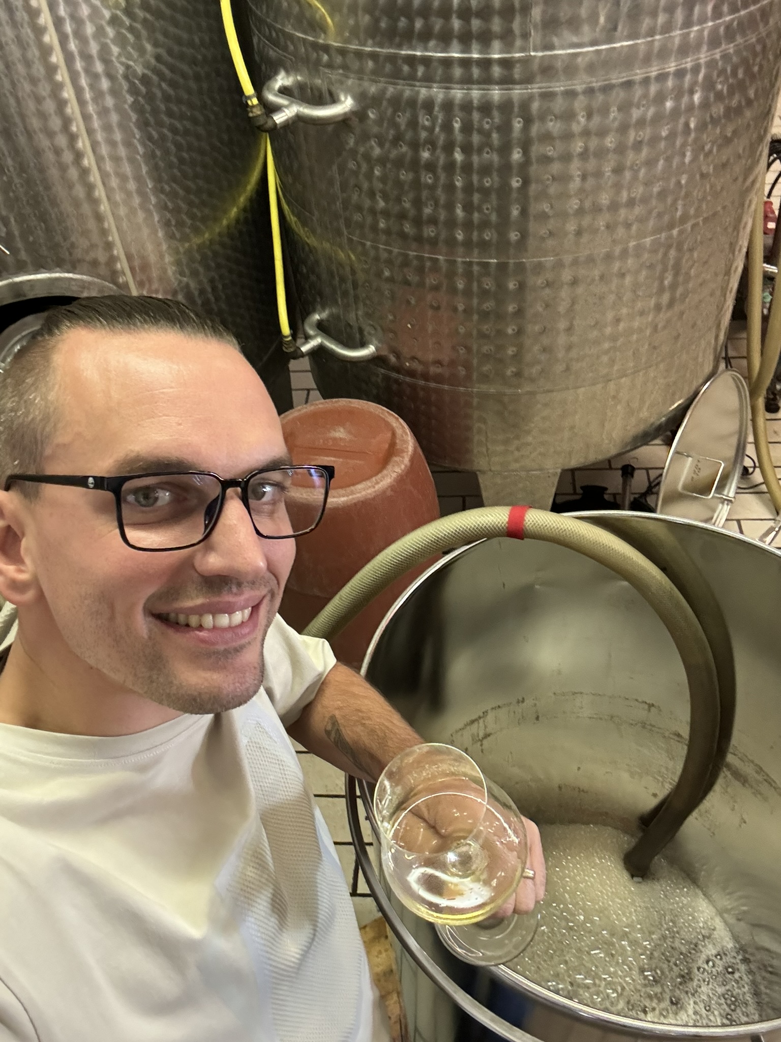 Nico mit einem Glas Weißwein direkt am Gärtank im Keller